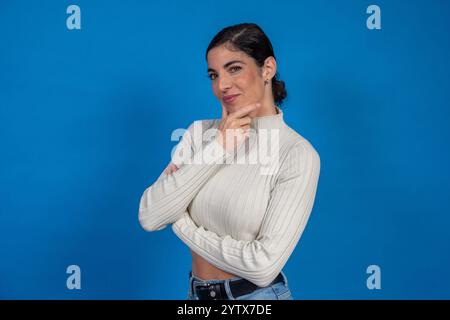 Portrait studio d'une jeune femme réfléchie avec les bras croisés touchant son menton sur un fond bleu vif Banque D'Images
