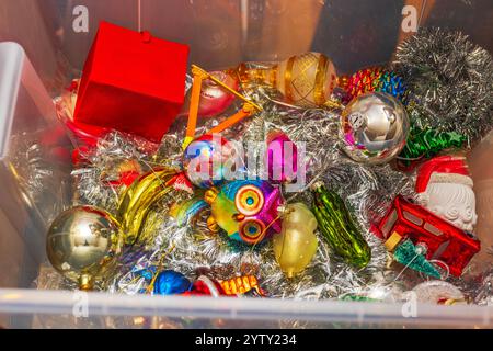 Ornements d'arbre de Noël lumineux et colorés stockés dans une boîte en plastique avec des guirlandes et des décorations festives. Banque D'Images