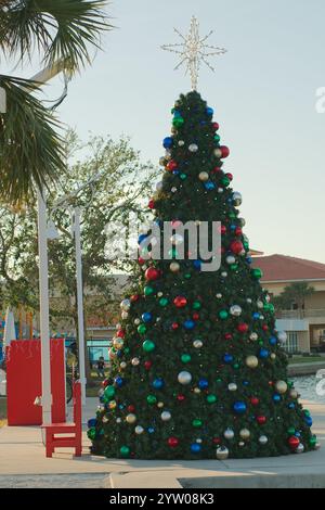 Vue verticale à un arbre de Noël décoré de boules rouges, blanches et vertes. À côté de Boca Ciega Bay à l'arrière. À St Pete Beach, FL. Ciel bleu et eau calme. Banque D'Images