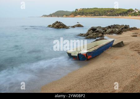 Un vieux bateau altéré se trouve abandonné sur une plage de sable, les vagues lançant doucement le rivage. La scène sereine évoque un sentiment de paix et de solitude. Banque D'Images