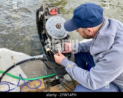 Un homme avec un camp de base réparant un moteur de bateau Banque D'Images