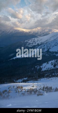 Remontée mécanique Alpine résortr avec des sièges qui passent au-dessus des pistes de ski de montagne au coucher du soleil par temps extrêmement venteux. Les gens sont méconnaissables. Banque D'Images