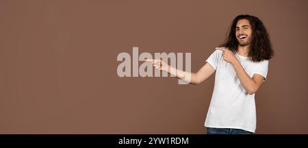 Jeune homme aux cheveux bouclés souriant et pointant dans un cadre isolé Banque D'Images