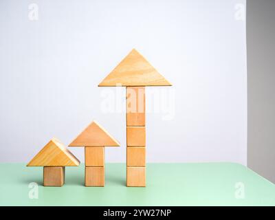 Grosse augmentation pointe de flèche en bois empilée sur le bloc de cube comme étapes de graphique à barres sur la table verte et le fond blanc. Les blocs de construction augmentent à mesure que le graphique d'investissement, Banque D'Images