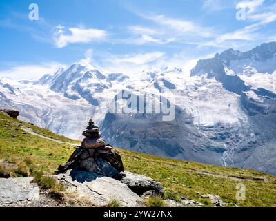 Cairn de rochers, roche empilée pagode zen sur la colline d'herbe verte sur le paysage de la montagne de neige vue et fond de ciel bleu dans les Alpes suisses à Zermatt, SWI Banque D'Images