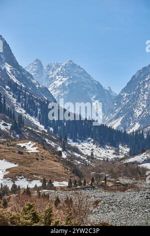 Paysage printanier niché dans une vallée de montagne majestueuse. Les sommets imposants, enveloppés de neige. Des parcelles de neige recouvrent les pentes, des arbres à feuilles persistantes, Banque D'Images