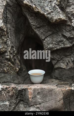 Une scène sereine et apaisante avec une tasse de thé délicate reposant doucement sur une surface rocheuse, symbolisant la vraie tranquillité Banque D'Images