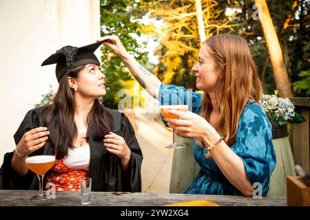Diplômé en casquette tenant un cocktail sourit à une femme dans une robe bleue lors d'une célébration en plein air, Bournemouth, Dorset Royaume-Uni Banque D'Images