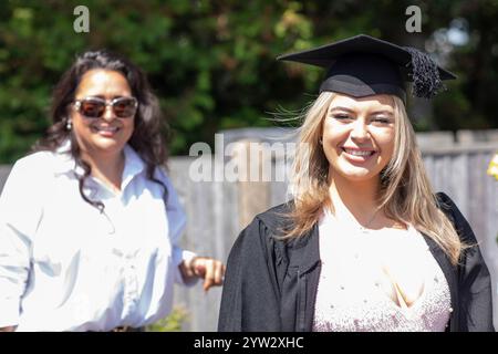 Une fière diplômée en casquette sourit brillamment le jour de sa remise des diplômes avec une autre femme debout à ses côtés, Bournemouth, Dorset UK Banque D'Images