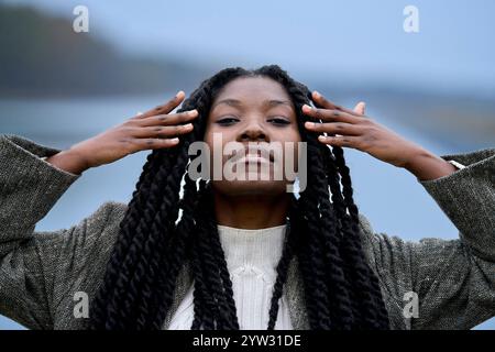 Une jeune femme sereine avec de longues tresses pose dehors, ses mains touchant gracieusement ses cheveux, Brandebourg, Allemagne Banque D'Images