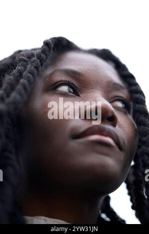 Jeune femme aux cheveux tressés regardant vers le haut avec une expression réfléchie sur un fond flou, Brandebourg, Allemagne Banque D'Images