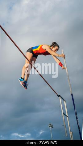 Voûte à perche féminine en plein air au-dessus de la barre contre un ciel nuageux. Banque D'Images