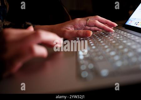 Gros plan de mains tapant sur un clavier d'ordinateur portable dans un environnement faiblement éclairé. Banque D'Images