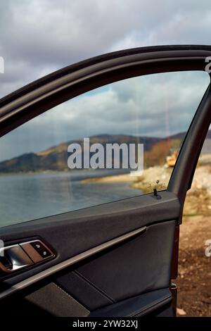 Porte de voiture ouverte avec une vue sur un paysage côtier pittoresque reflété dans sa fenêtre, sous un ciel nuageux, Highlands, Écosse Banque D'Images