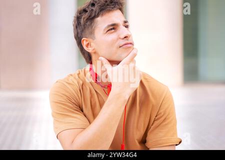 Jeune homme réfléchi avec casque rouge dans un cadre extérieur lumineux Banque D'Images