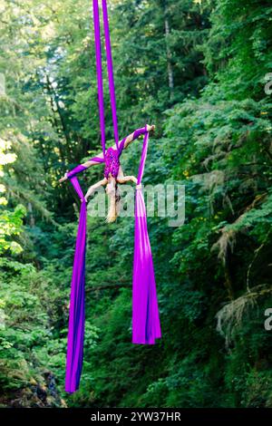 L'artiste aérien est suspendu à l'envers dans des soies violettes vibrantes au milieu d'une forêt luxuriante, aux États-Unis Banque D'Images