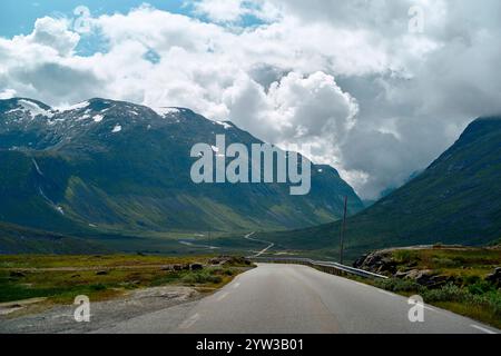 Route sinueuse à travers une vallée verdoyante majestueuse avec des montagnes imposantes sous un ciel dynamique, Trollstiege, Trollvegen, Norvège Banque D'Images