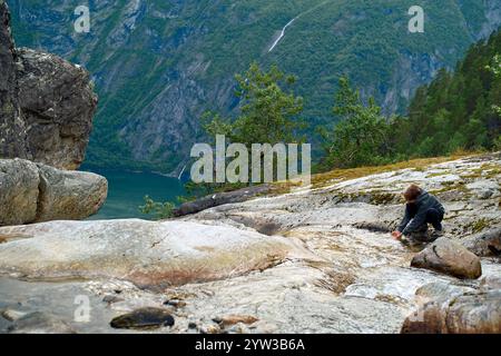 Adolescent sur une pente rocheuse surplombant un fjord profond avec des falaises abruptes et une cascade lointaine, buvant de l'eau claire, Storfjorden, Norvège Banque D'Images