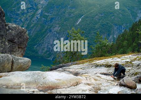 Adolescent sur une pente rocheuse surplombant un fjord profond avec des falaises abruptes et une cascade lointaine, buvant de l'eau claire, Storfjorden, Norvège Banque D'Images