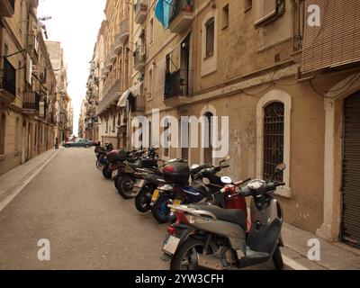 Une rue étroite bordée de motos garées sur le trottoir et d'immeubles d'appartements classiques avec balcons dans une ville européenne, Barcelone, Espagne Banque D'Images
