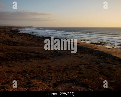 Coucher de soleil sur une plage sereine avec des vagues douces, soulignant le contraste entre le rivage de sable et le vaste océan, Fuerteventura, Espagne Banque D'Images