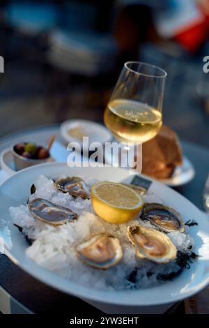 Huîtres fraîches sur glace avec citron accompagnées d'un verre de vin blanc, de pain et d'olives sur une table en plein air, rivière Moselle, Allemagne Banque D'Images