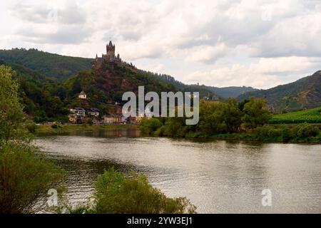 Vue panoramique d'une rivière avec un château au sommet d'une colline entourée de verdure et un village pittoresque ci-dessous sous un ciel nuageux, la Moselle, Allemagne Banque D'Images