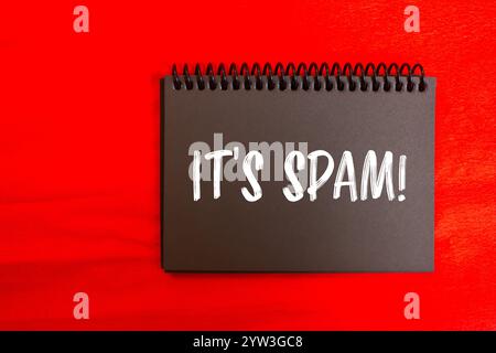 C'est un message spam écrit sur la page noire du carnet de notes avec un fond rouge. Conceptuel, c'est le symbole spam. Copier l'espace. Banque D'Images