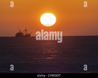 Silhouette d'un bateau de pêche contre un coucher de soleil orange vibrant sur l'océan, bateau chalutier coucher de soleil nord île de la mer de Texel Banque D'Images