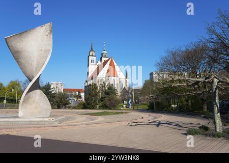 Sculpture moderne devant une église avec des tours et des arbres en arrière-plan, Monument de l'amitié entre les peuples et l'église Saint-Jean, Magdebourg Banque D'Images