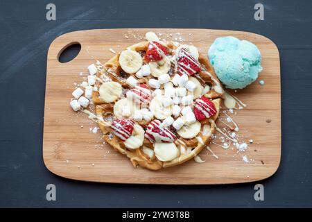 Délicieuse gaufre à la banane et à la fraise servie avec de la crème glacée et un filet de sauce au chocolat blanc Banque D'Images
