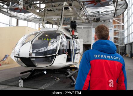 09 décembre 2024, Bavière, Bad Tölz : un membre de la Bavarian Mountain Rescue se tient devant un modèle d'hélicoptère dans le Mountain Rescue Center for Safety and Training. Des exercices sont présentés lors de l’événement organisé par Tourismus Oberbayern München avec des représentants du service de secours en montagne, du club alpin allemand, du service de secours en eau et d’autres organisations. Photo : Magdalena Henkel/dpa Banque D'Images