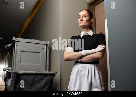 Jeune femme dans une tenue élégante se tient avec confiance dans un couloir bien éclairé, exsudant le charisme. Banque D'Images