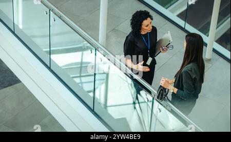 Une vue en grand angle montre deux collègues qui discutent dans un environnement de bureau contemporain. La conversation semble professionnelle, avec un ho Banque D'Images
