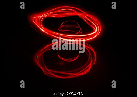 Traînées de lumière rouge abstraites créées par la peinture lumineuse autour d'une boule de verre statique posée sur un miroir sur un fond noir Uni Banque D'Images