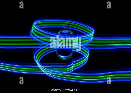 Traînées de lumière bleue et verte abstraites créées par la peinture à la lumière autour d'une boule de verre statique posée sur un miroir sur un fond noir Uni Banque D'Images