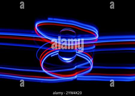 Traînées de lumière rouge et bleue abstraites créées par la peinture à la lumière autour d'une boule de verre statique posée sur un miroir sur un fond noir Uni Banque D'Images