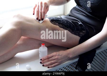 Jeune femme appliquant des médicaments à ses ecchymoses assis sur le rebord de la fenêtre Banque D'Images