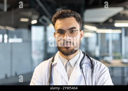 Un médecin confiant portant des lunettes et un stéthoscope pose dans un environnement de bureau. Parfait pour les soins de santé, la médecine ou les profils professionnels mettant en vedette les professionnels de la santé dans un cadre contemporain. Banque D'Images