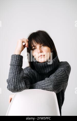 Jeune femme souriant dans un pull confortable, mode hivernale décontractée, style minimaliste, chaud et confortable, énergie positive, portrait intérieur décontracté. Banque D'Images