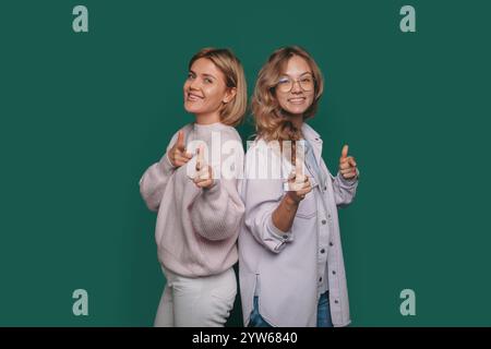 Deux femmes extrêmement élégantes posent gaiement et avec confiance sur un fond vert vif Banque D'Images