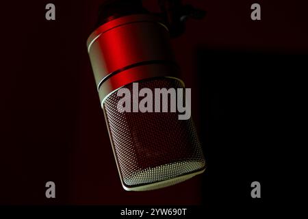 Microphone studio avec éclairage rouge sur fond sombre. Gros plan d'un microphone à condensateur professionnel pour l'enregistrement et le podcasting. Concept de production musicale et audio. Banque D'Images