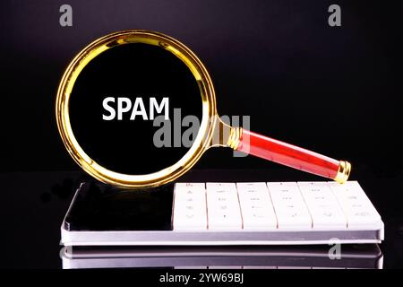 Une loupe dorée met en évidence le mot spam sur un fond noir. En dessous, un clavier téléphonique blanc est visible, soulignant le thème de Banque D'Images