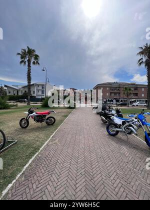 Porto Sant'Elpidio, Italie - 06 juillet 2022 : une rangée de motos stationnées longe un sentier urbain ensoleillé bordé de palmiers. Bâtiments résidentiels stan Banque D'Images