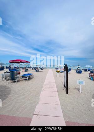 Porto Sant'Elpidio, Italie - 06 juillet 2022 : une plage de sable tranquille avec un chemin dégagé menant à des chaises longues sous des parasols bleus. Un réglage parfait pour Banque D'Images