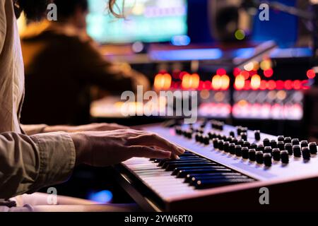 Musicien masculin exécutant une chanson à succès sur clavier électronique en studio d'enregistrement, jouant des notes sur contrôleur midi pour éditer en post-production. Artiste chantant dans la salle de contrôle. Gros plan. Banque D'Images