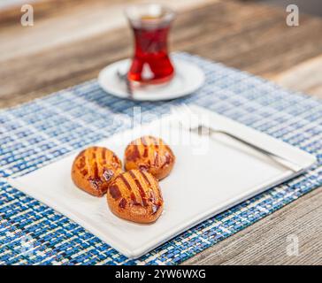 Dessert turc traditionnel avec thé : Sekerpare. Sekerpare est servi avec du thé sur une assiette blanche. Banque D'Images