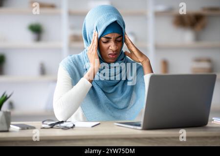 Concept de mal de tête. Femme indépendante musulmane noire en relief souffrant de migraine sur le lieu de travail Banque D'Images