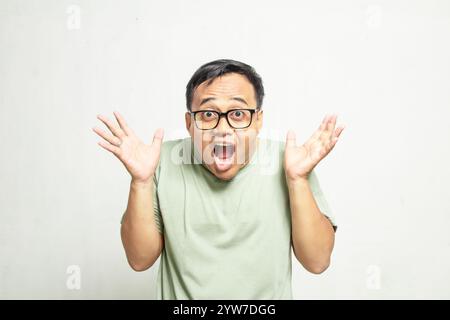 Visage surpris de l'homme bespectacled asiatique heureux indonésien portant chemise vert mousse sur fond blanc. Banque D'Images