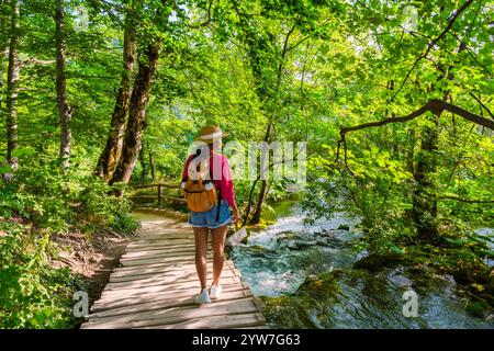 Un voyageur serpente le long d'un chemin en bois entouré de verdure vibrante et d'eaux en cascade, immergé dans la beauté enchanteresse du parc national des lacs de Plitvice en Croatie pendant l'été Banque D'Images